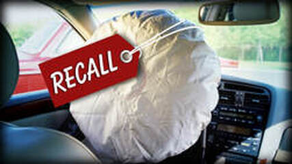White airbag inflated on driver's side with red sticker around it that says recall